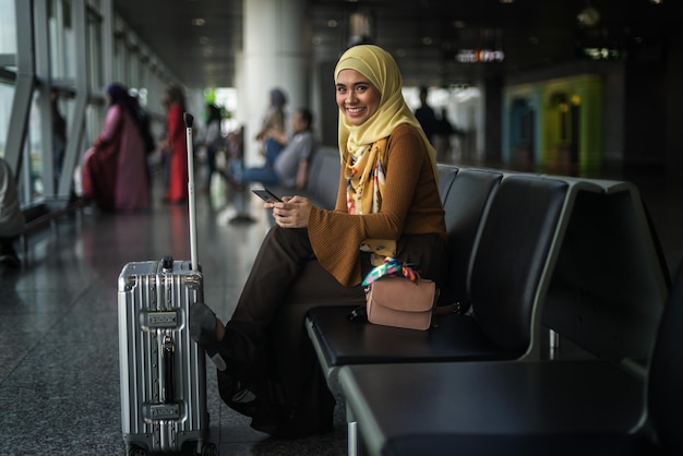Ritratto di una donna con un telefono cellulare mentre è seduta accanto alla valigia all'aeroporto