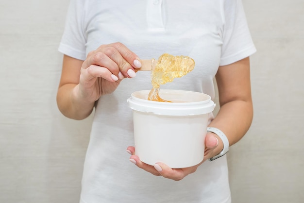 Ritratto di una donna con un vasetto di pasta di zucchero per zuccherareEstetista con in mano un vasetto di pasta di zucchero per shugaring su sfondo bianco