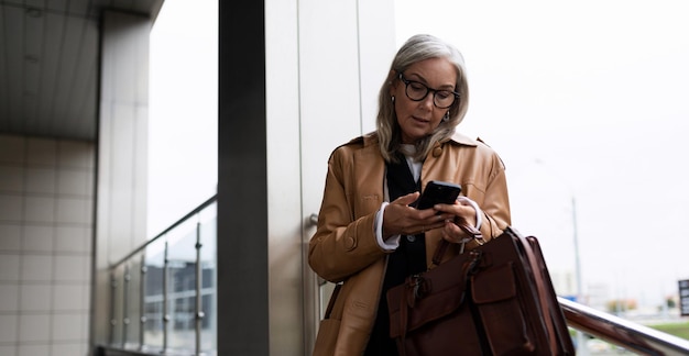 Ritratto di una donna d'affari alla moda dai capelli grigi matura con un telefono cellulare nelle sue mani al