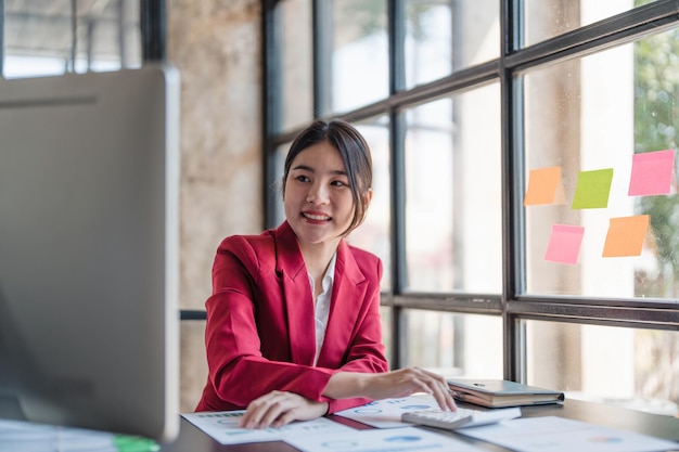 Ritratto di una donna d'affari asiatica sorridente che si gode il suo lavoro sul suo computer portatile in ufficio