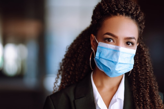 Ritratto di una donna d'affari che indossa una maschera protettiva e guarda a porte chiuse.