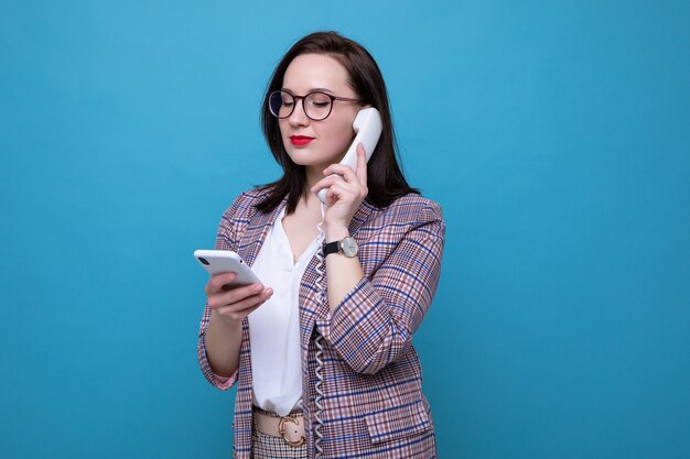 Ritratto di una donna d'affari che sta parlando al telefono dell'ufficio e che tiene uno smartphone in mano