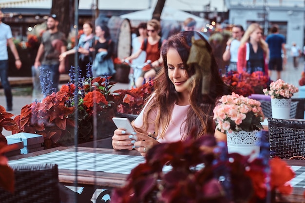 Ritratto di una donna d'affari di mezza età con lunghi capelli castani che utilizza uno smartphone mentre si siede al caffè all'aperto.