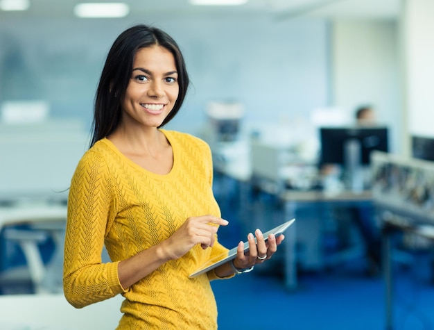 Ritratto di una donna d'affari felice in maglione in piedi con un tablet in ufficio