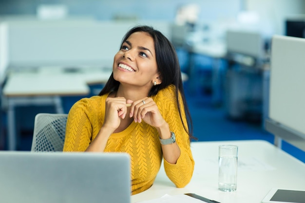 Ritratto di una donna d'affari felice seduta al suo posto di lavoro in ufficio e guardando in alto