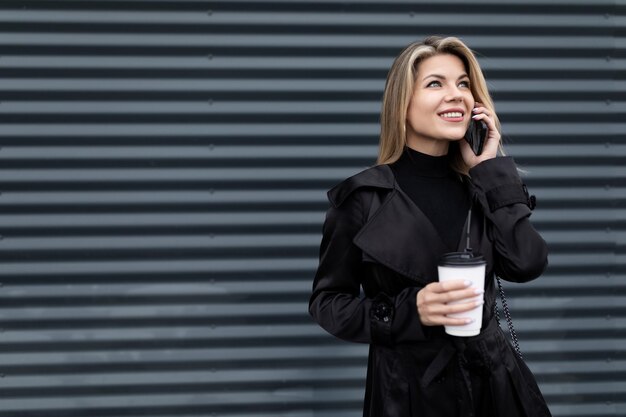 Ritratto di una donna d'affari in abiti eleganti d'affari con una tazza di caffè che parla su un cellulare