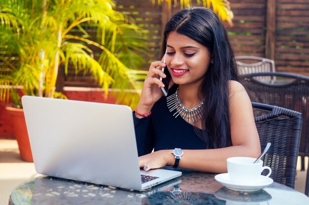 Ritratto di una donna d'affari indiana felice che lavora al computer portatile al caffè d'estate