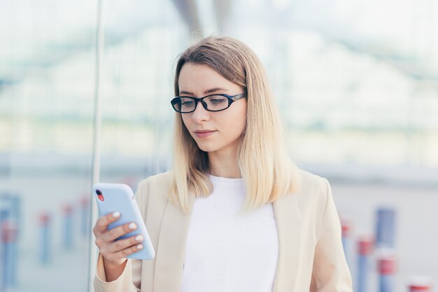 Ritratto di una donna d'affari seria con gli occhiali bionda legge le notizie da un telefono cellulare utilizza l'applicazione per riscrivere i messaggi