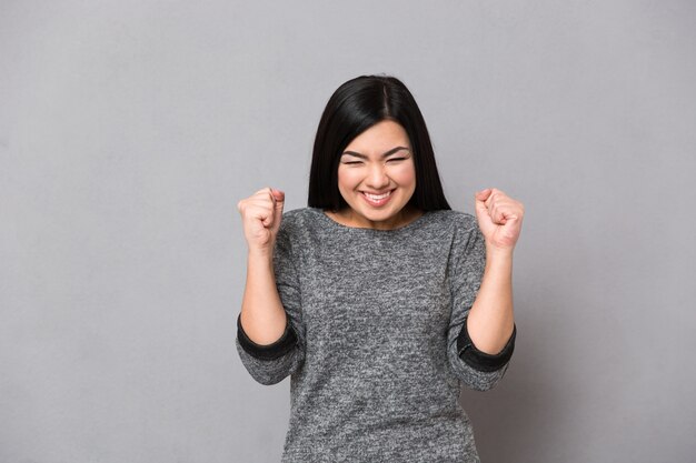 Ritratto di una donna felice che celebra il suo successo sul muro grigio