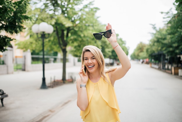 Ritratto di una donna felice che parla sul telefono cellulare e che fluttua alla via della città.