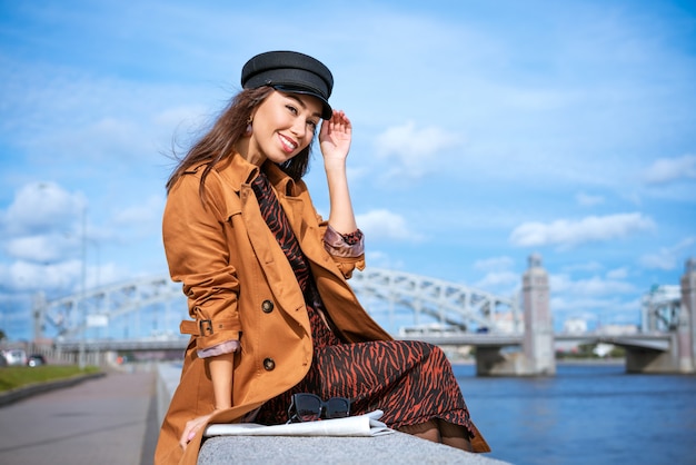 Ritratto di una donna felice sull'argine del fiume in un berretto nero e giacca marrone in una giornata di sole