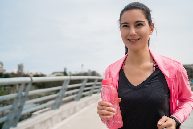 Ritratto di una donna fitness in esecuzione e con in mano una bottiglia d'acqua all'aperto in strada. Sport e stile di vita sano.