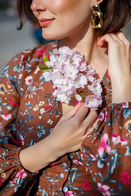 Ritratto di una donna gentile sullo sfondo di fiori di sakura. Passeggia nel giardino fiorito di sakura. Giovane donna alla moda che sta nel parco di sakura e che gode della bellezza