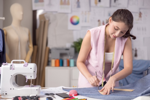 Ritratto di una donna giovane e attraente sul tavolo di uno stilista alla moda, circondata da campioni di tessuti colorati. Donna attraente che lavora in uno studio di moda con manichini e panni colorati.