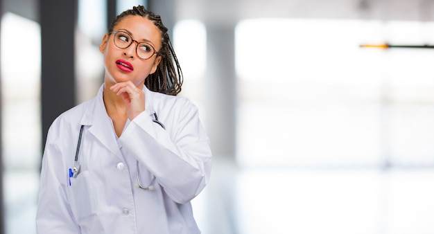 Ritratto di una donna giovane medico nero pensando e alzando lo sguardo, confuso su un&#39;idea