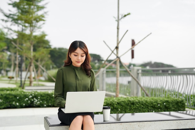 Ritratto di una donna impegnata nelle vendite seduta al business park e usando il suo laptop mentre scrive testo sul cellulare Imprenditrice che lavora online.