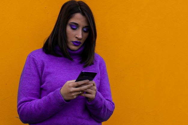 Ritratto di una donna in abito viola e trucco in chat con un telefono cellulare su sfondo giallo