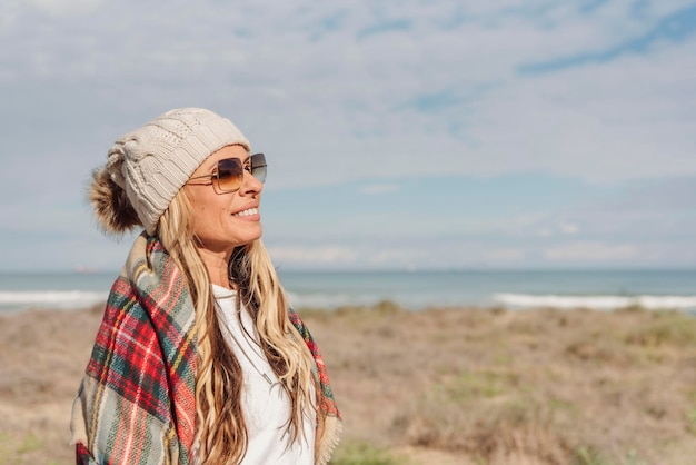 Ritratto di una donna in cappello bobble invernale lavorato a maglia che si gode una soleggiata giornata invernale o autunnale in spiaggia