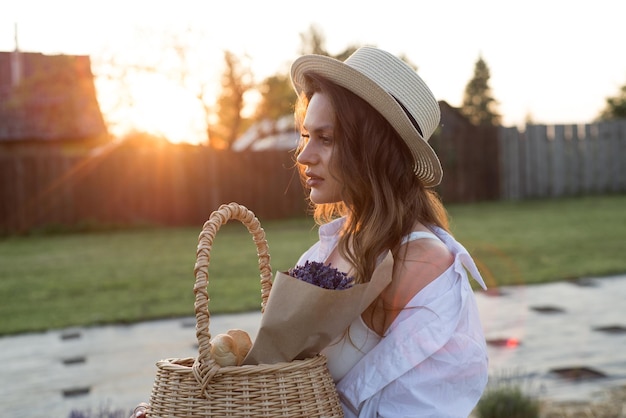 Ritratto di una donna in cappello di paglia al tramonto con bouquet di lavanda in un cestino