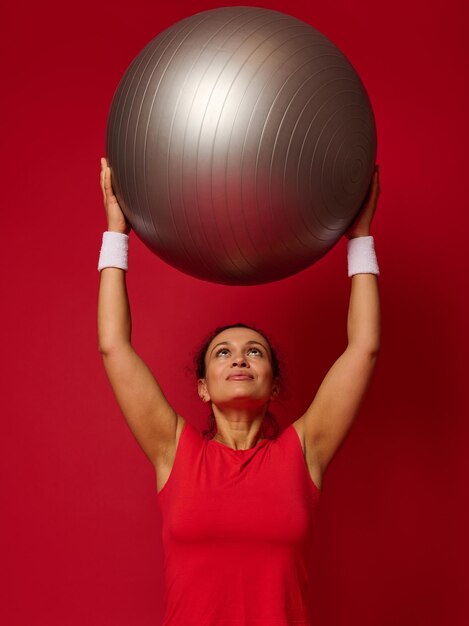 Ritratto di una donna in forma felice fitness in piedi in possesso di una palla in forma nelle sue braccia sollevate sopra la sua testa Copia spazio libero per il testo