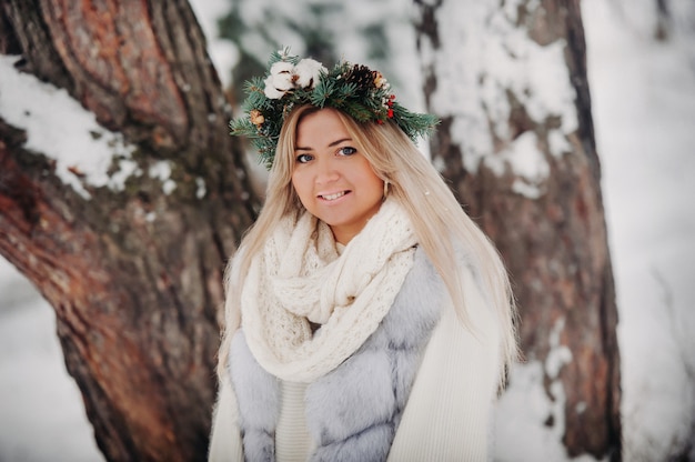 Ritratto di una donna in una pelliccia bianca in una foresta di inverno freddo. Ragazza con una ghirlanda in testa in una foresta invernale innevata.