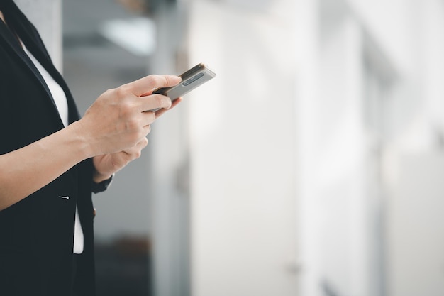 Ritratto di una donna lavoratrice asiatica che indossa un abito nero con in mano un telefono cellulare connesso a Internet per inviare informazioni sul lavoro. Concetto di utilizzo della tecnologia Internet nella vita quotidiana