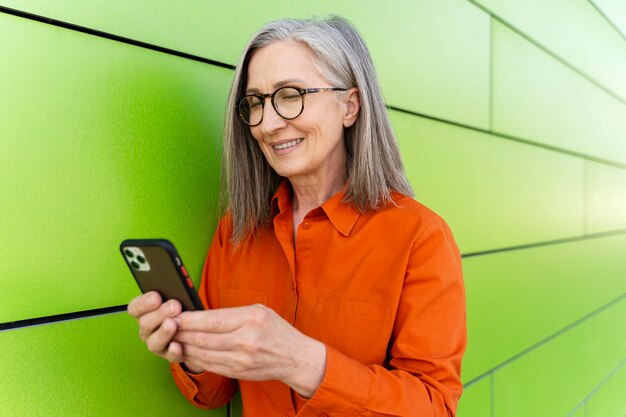 Ritratto di una donna matura dai capelli grigi sorridente che tiene lo smartphone utilizzando l'app mobile facendo acquisti online in piedi per strada Felice donna di 60 anni che legge la tecnologia di comunicazione dei messaggi di testo