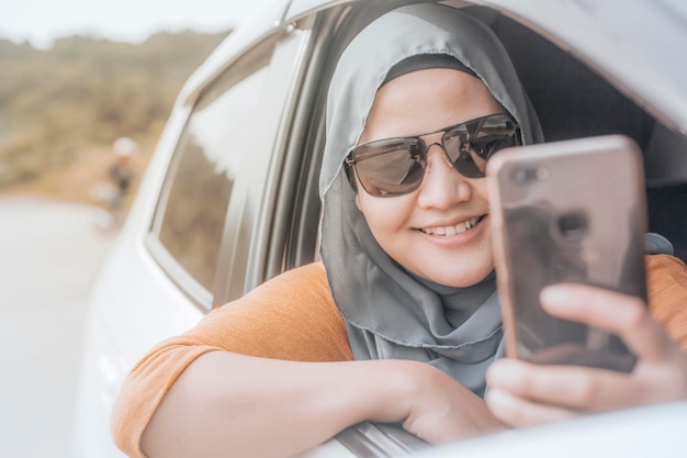 Ritratto di una donna musulmana asiatica che sorride mentre scatta un selfie con lo smartphone nella sua auto