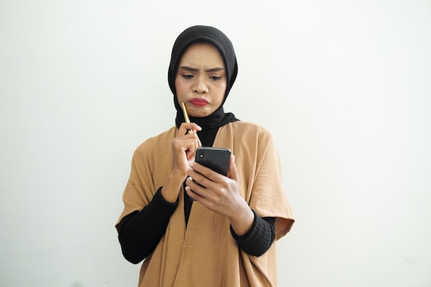 Ritratto di una donna musulmana asiatica dal pensiero felice che indossa l'hijab che effettua una chiamata con un telefono cellulare