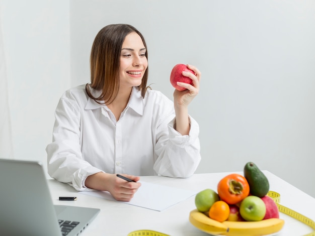 Ritratto di una donna nutrizionista seduta a un tavolo con la frutta.