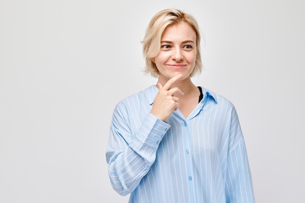 Ritratto di una donna pensierosa con un sorriso sottile che indossa una camicia blu su uno sfondo chiaro