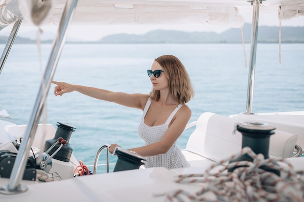 Ritratto di una donna seria ricca e sicura di sé seduta al volante del suo yacht e che punta la mano di lato. Sullo sfondo di acqua e natura. Stile di vita casual