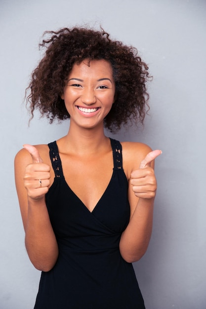 Ritratto di una donna sorridente che mostra il pollice in su sopra il muro grigio