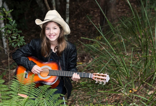 Ritratto di una donna sorridente che suona la chitarra mentre è seduta accanto alla pianta