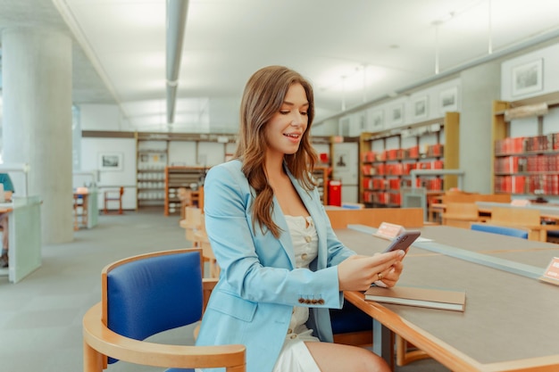 Ritratto di una donna sorridente con un telefono cellulare che usa un'app mobile che lavora in una biblioteca