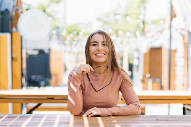 Ritratto di una donna sorridente felice che tiene gli occhiali da sole in città in estate in un caffè e aspetta f