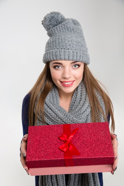 Ritratto di una donna sorridente in panno invernale che dà scatola regalo in telecamera isolata su uno sfondo bianco white