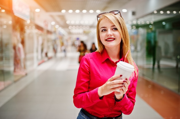 Ritratto di una donna splendida in camicia rossa e jeans in possesso di una tazza di caffè in un centro commerciale.