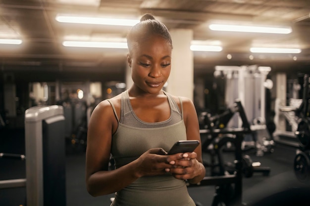 Ritratto di una donna sportiva nera in forma in palestra che scrive messaggi al telefono