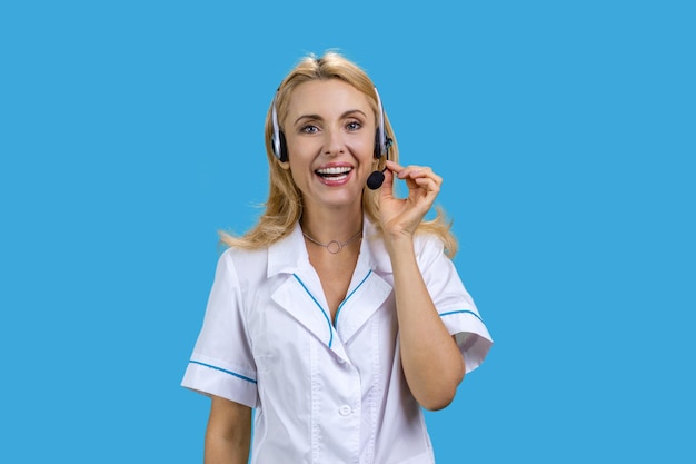 Ritratto di una dottoressa bionda matura che indossa un auricolare isolato sul blu