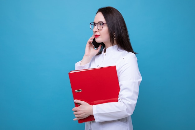 Ritratto di una dottoressa con una cartella rossa, parlando al telefono su sfondo blu