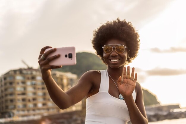 Ritratto di una elegante donna africana che agita durante una videochiamata accanto al mare