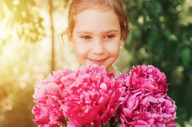 ritratto di una felice bambina caucasica di sette anni, tiene in mano un mazzo di peonia rosa