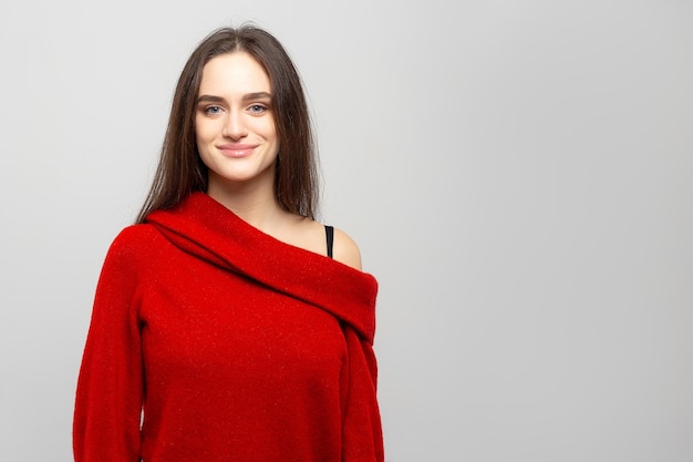 Ritratto di una giovane bella donna con un sorriso leggero vestito con un maglione rosso su sfondo grigio chiaro