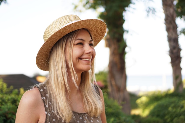 Ritratto di una giovane bionda con un cappello su uno sfondo tropicale. Luce solare e colori brillanti.