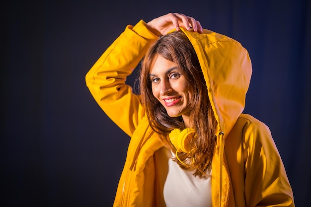 Ritratto di una giovane bruna caucasica con cuffie e giacca gialla su sfondo nero, bella ragazza che sorride alla telecamera