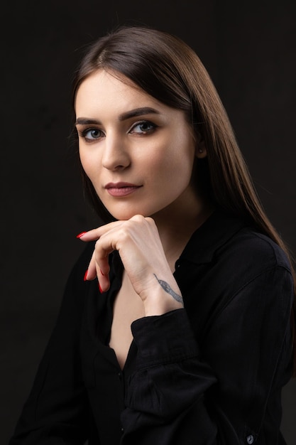 Ritratto di una giovane bruna con i capelli lunghi in studio Foto drammatica in colori scuri Una ragazza con un tatuaggio di serpente sul braccio