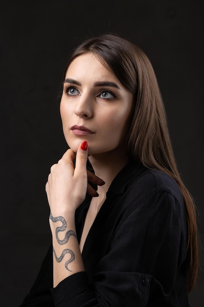 Ritratto di una giovane bruna con i capelli lunghi in studio Foto drammatica in colori scuri Una ragazza con un tatuaggio di serpente sul braccio