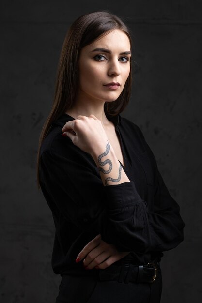 Ritratto di una giovane bruna con i capelli lunghi in studio Foto drammatica in colori scuri Una ragazza con un tatuaggio di serpente sul braccio