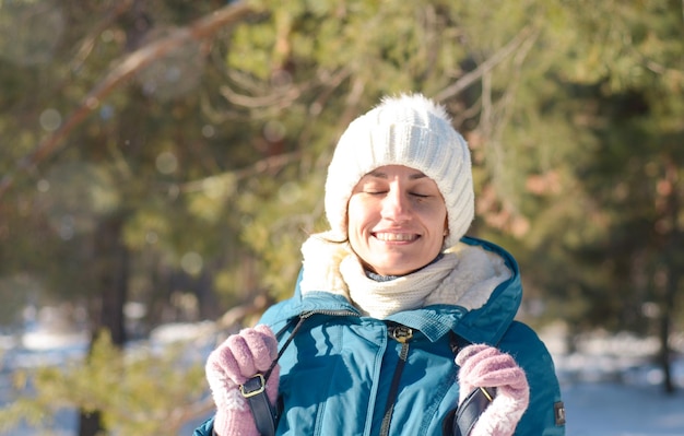 Ritratto di una giovane brunetta felice in abiti invernali in un cappello lavorato a maglia bianco nel gelo al sole